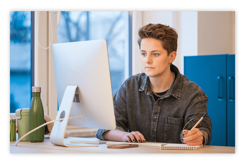 A person taking notes from laptop whilst sitting at a desk.