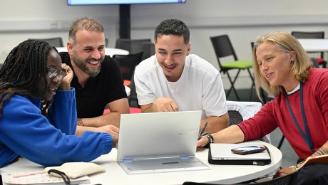Four adult learners sitting around a table looking at a laptop.