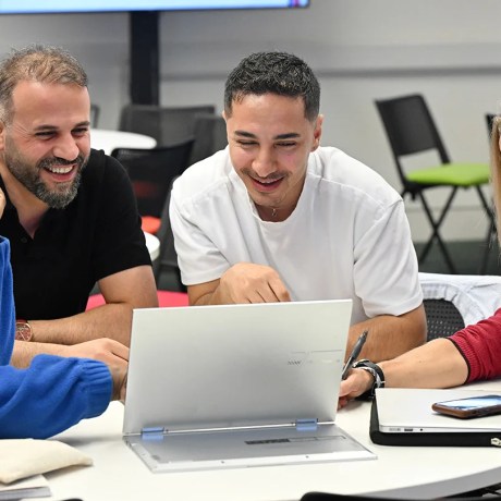 Four adult learners sitting around a table looking at a laptop.